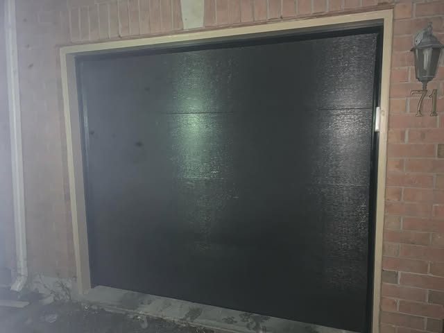 Matte black single garage door installed in a brick opening