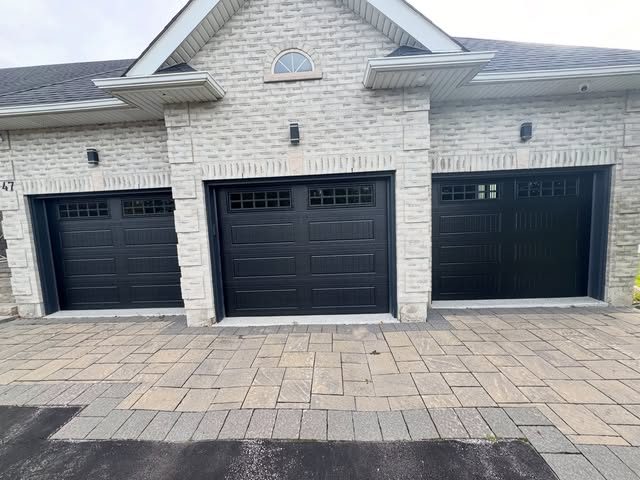 Three matte black carriage-style garage doors installed on a stone home